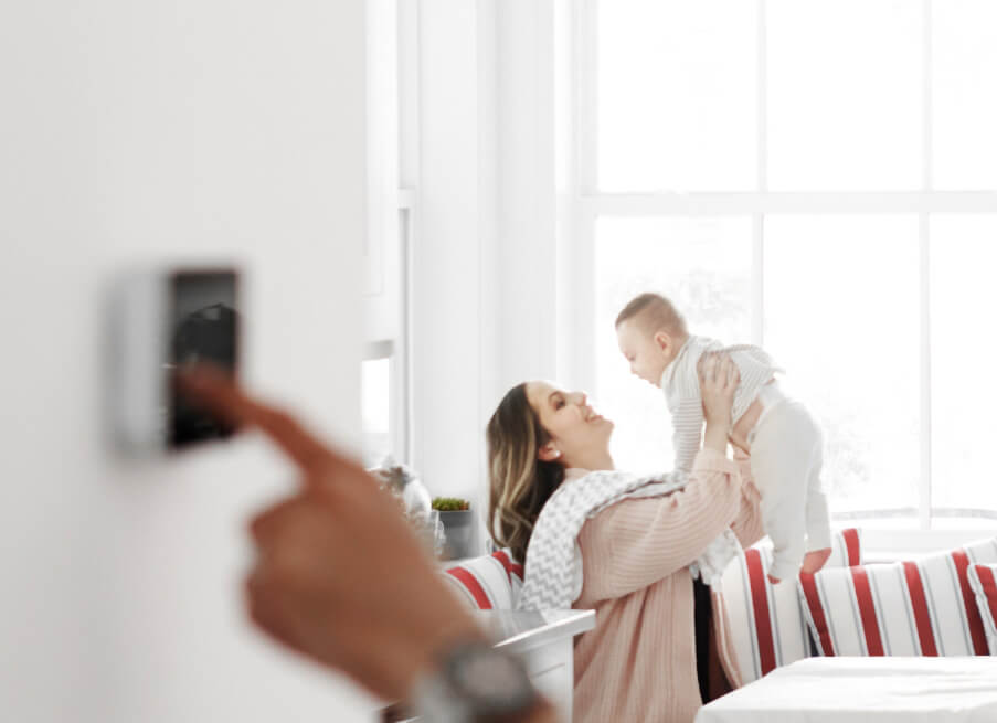 Femme avec son bébé pendant qu’une personne règle la température sur le thermostat